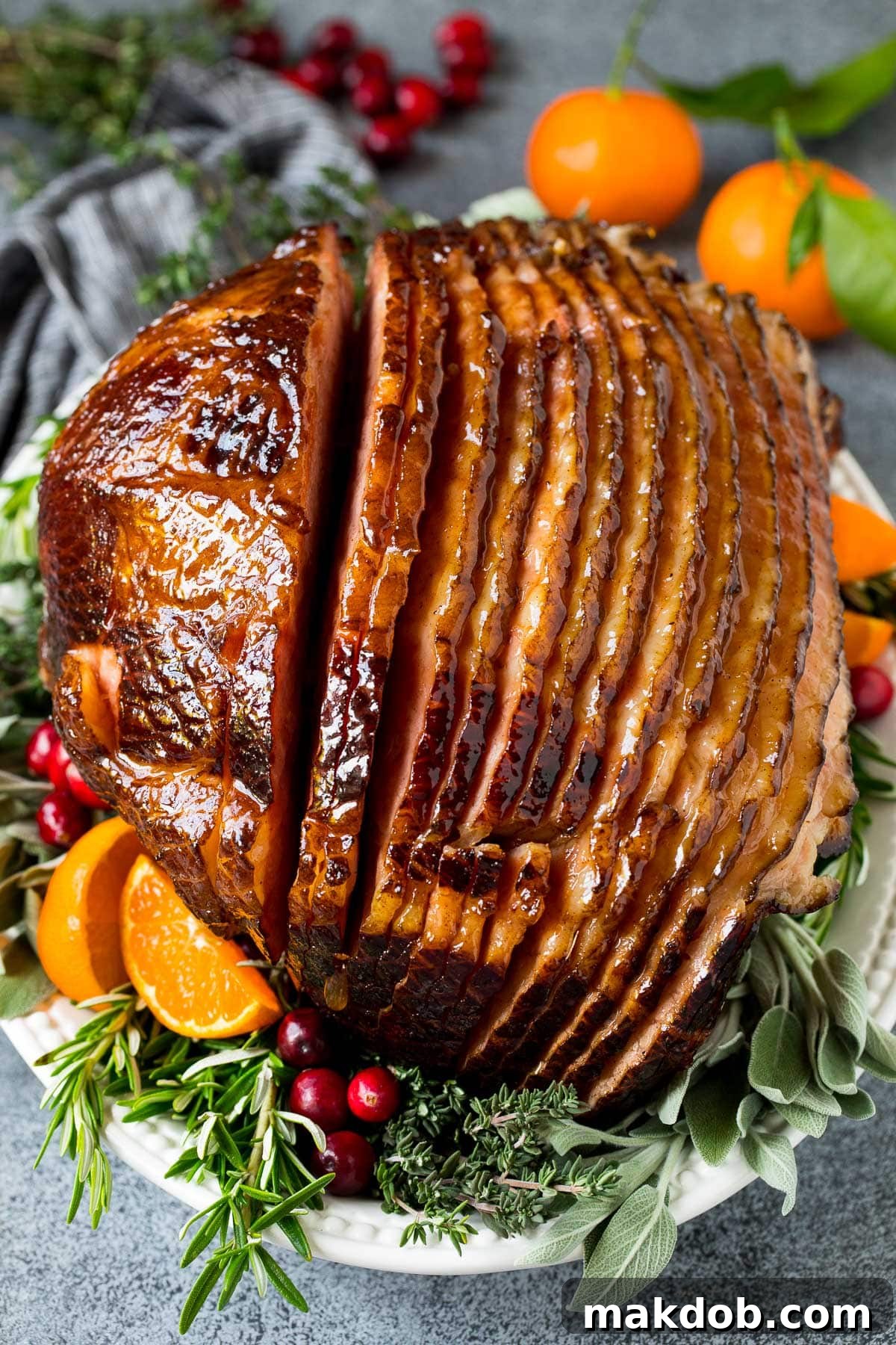 Baked ham coated in glaze, served on a platter with herbs and fruit.