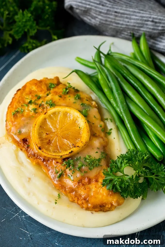 Chicken Francese served over creamy mashed potatoes with a side of fresh green beans, garnished with lemon.