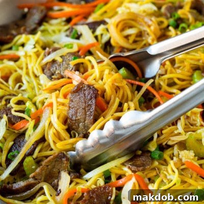 Tongs serving up a portion of beef chow mein.