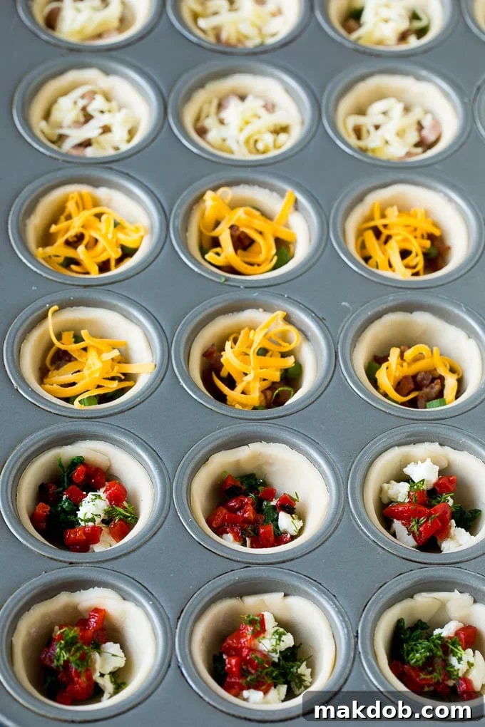 Mini Quiche Recipe #eggs #breakfast #brunch #appetizer #dinneratthezoo Muffin tins filled with individual pie crusts, a variety of vegetables, savory meats, and shredded cheese, ready for the egg mixture.