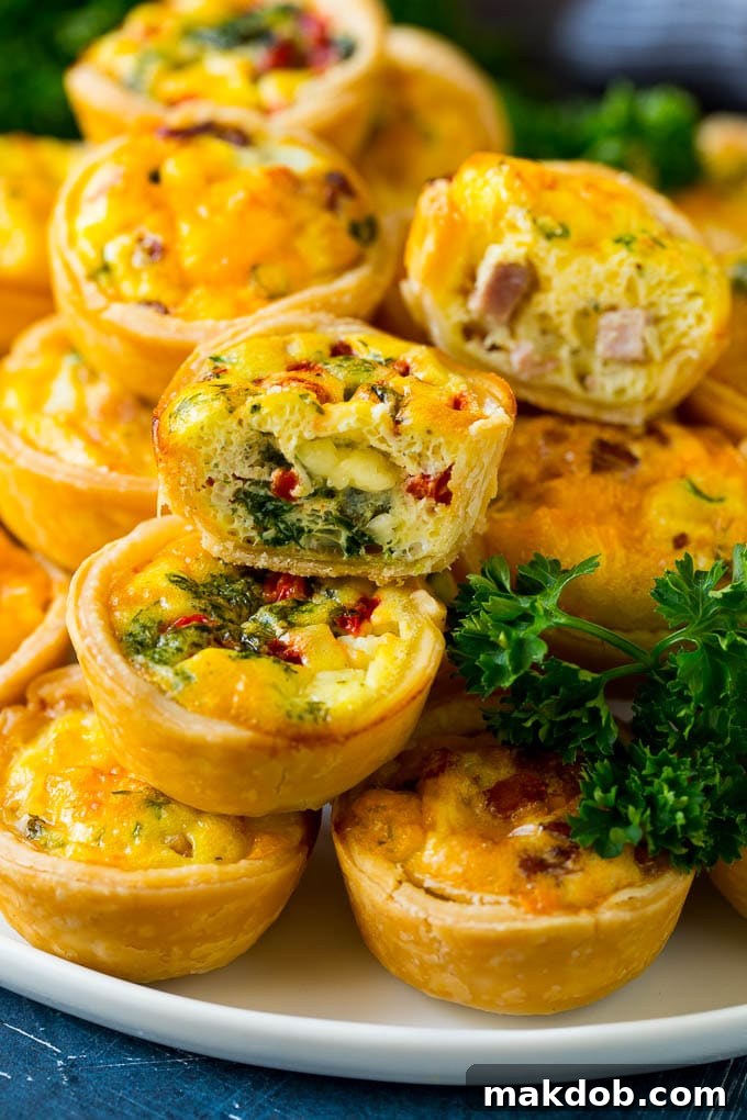 Mini Quiche Recipe #eggs #breakfast #brunch #appetizer #dinneratthezoo A vibrant serving platter artfully arranged with various mini quiches, some cut in half to reveal their colorful and diverse fillings.