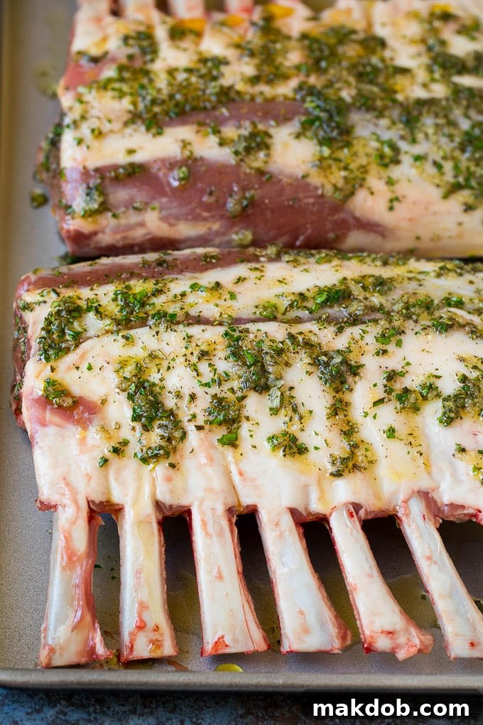 A mixture of olive oil, minced garlic, and fresh herbs being generously drizzled over a rack of lamb, ready for seasoning.