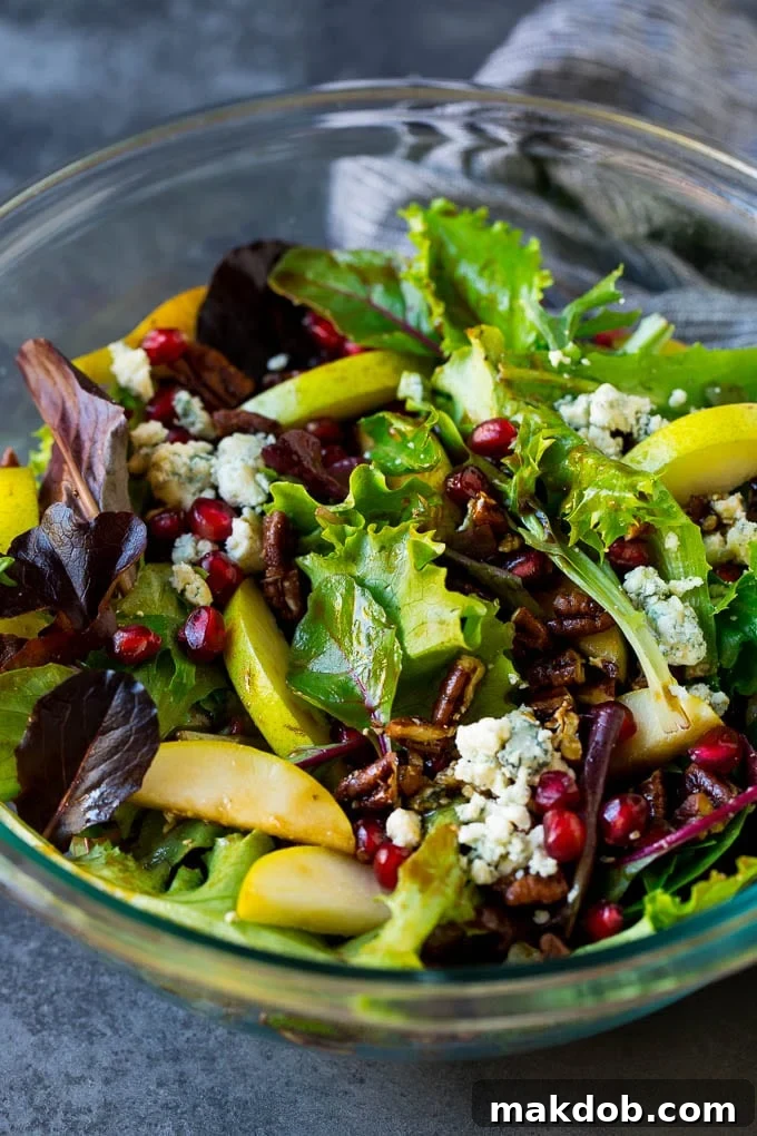 A bowl of pear salad with pomegranate, blue cheese and candied pecans, showcasing vibrant colors and textures.