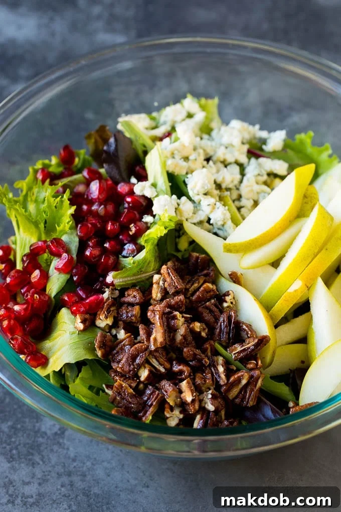 A vibrant mix of lettuce with thinly sliced pears, crumbled blue cheese, and chopped pecans layered on top.