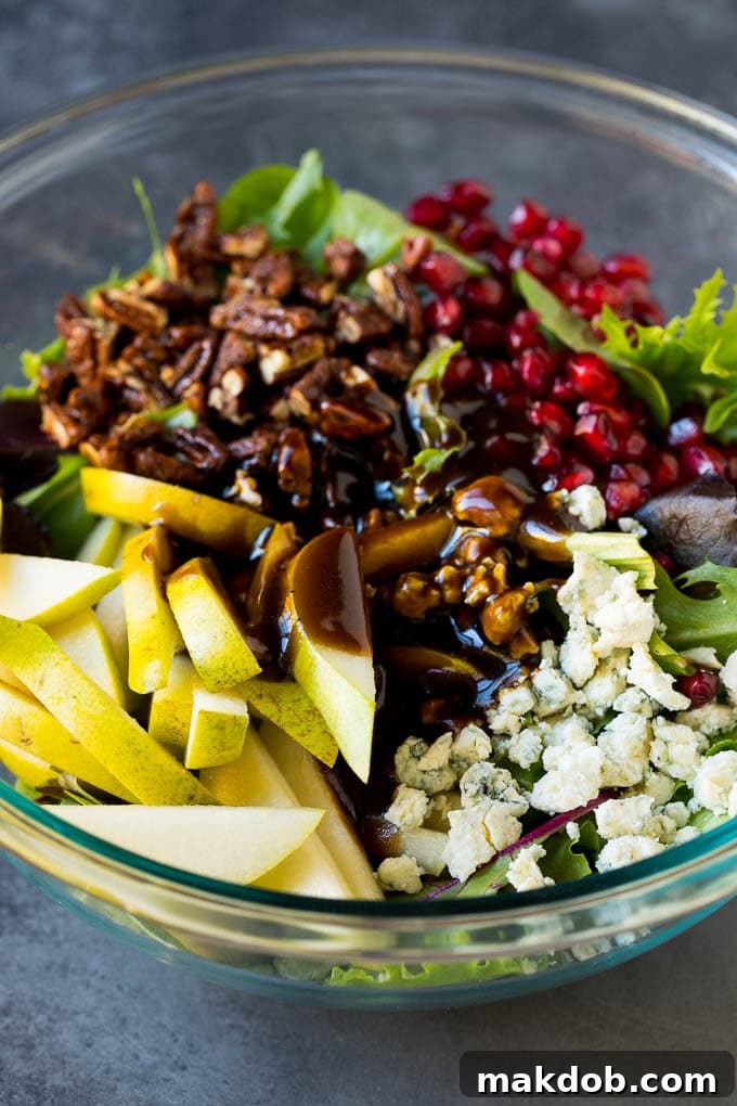 Homemade balsamic dressing being drizzled over a bowl of mixed greens, fruit, and vibrant pomegranate seeds.