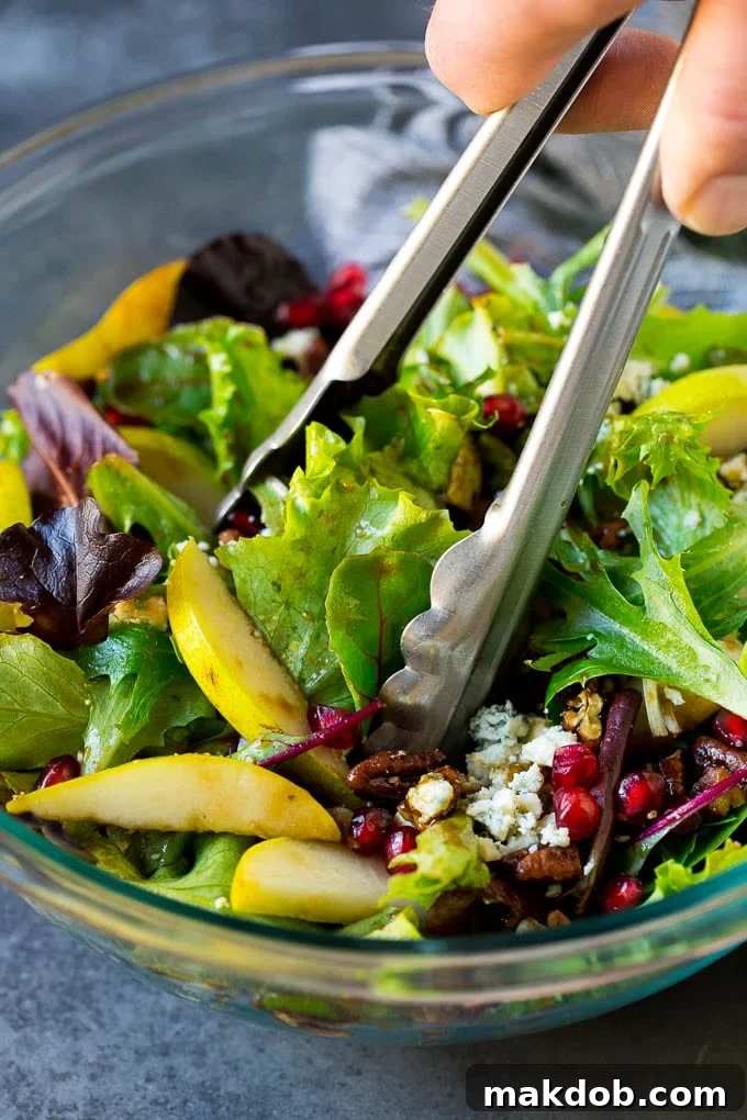 Serving up a portion of freshly tossed pear salad with tongs, ready to enjoy.