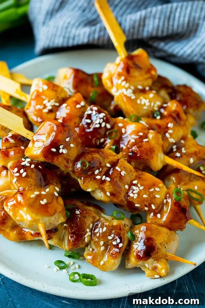 Homemade Chicken Yakitori Recipe | Japanese Grilled Chicken Skewers A plate of perfectly grilled chicken yakitori skewers, glistening with a sweet and savory glaze, garnished with fresh sesame seeds and thinly sliced green onions.