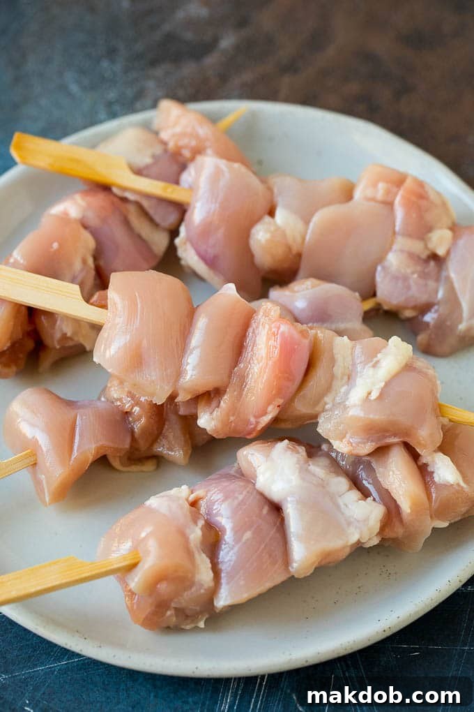 Chicken Skewers Ready for Grilling | Yakitori Recipe Step Raw chicken thigh pieces, uniformly cut into bite-sized cubes, meticulously threaded onto wooden skewers, ready for grilling.
