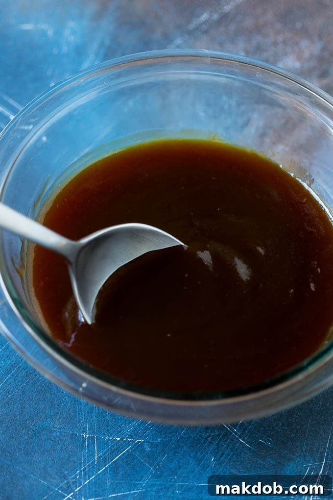 Homemade Yakitori Glaze | Sweet and Savory Sauce A small glass mixing bowl filled with a dark, glossy, sweet and savory yakitori sauce, ready for basting.