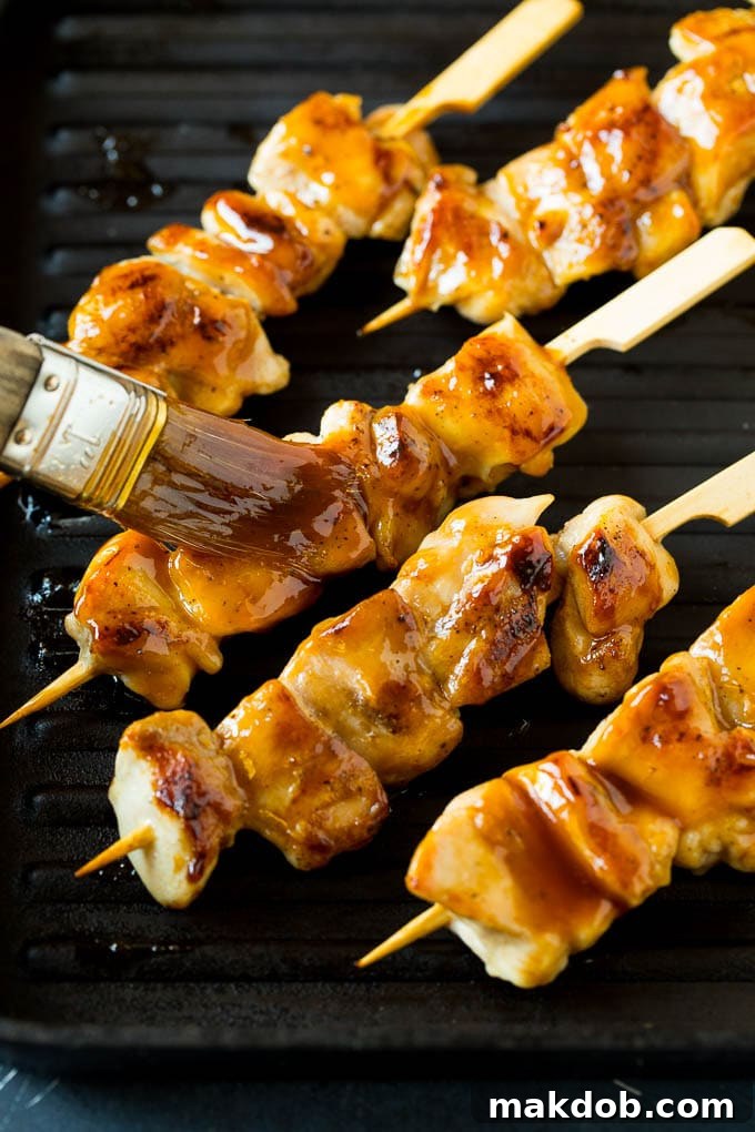 Glazing Chicken Yakitori on the Grill A basting brush applying a generous layer of sweet and savory yakitori glaze onto sizzling grilled chicken skewers.