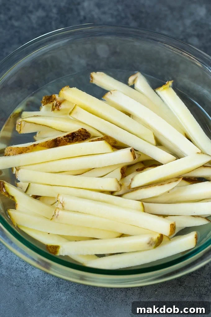 Freshly cut Russet potato sticks soaking in a bowl of cold water, a crucial step for removing excess starch and ensuring crispiness.