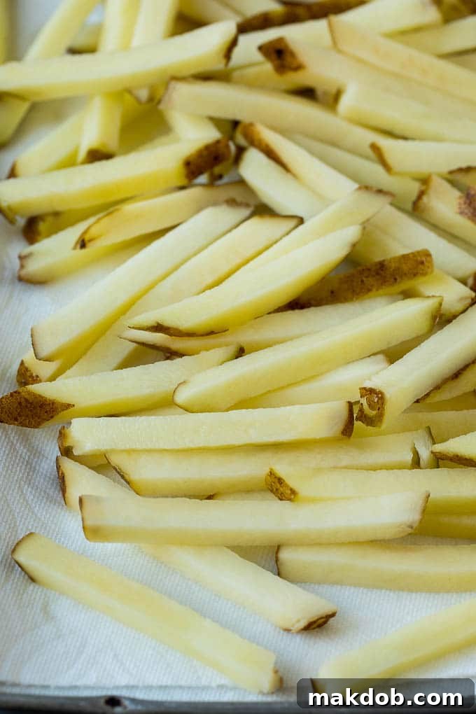 Uniformly cut potato sticks neatly arranged on a paper towel-lined baking sheet, waiting to be fried. This image emphasizes the importance of drying the potatoes before cooking.