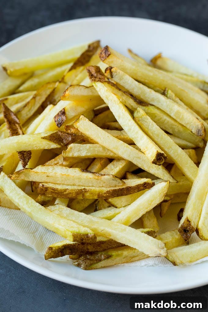 A plate of par-fried potato sticks, lightly cooked and ready for their second fry, demonstrating the intermediate stage of the double-frying process.