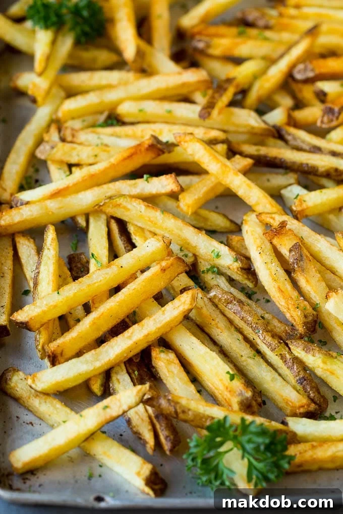 A generous serving of homemade French fries cooling on a sheet pan lined with paper towels, showcasing their beautiful golden color and crisp texture.