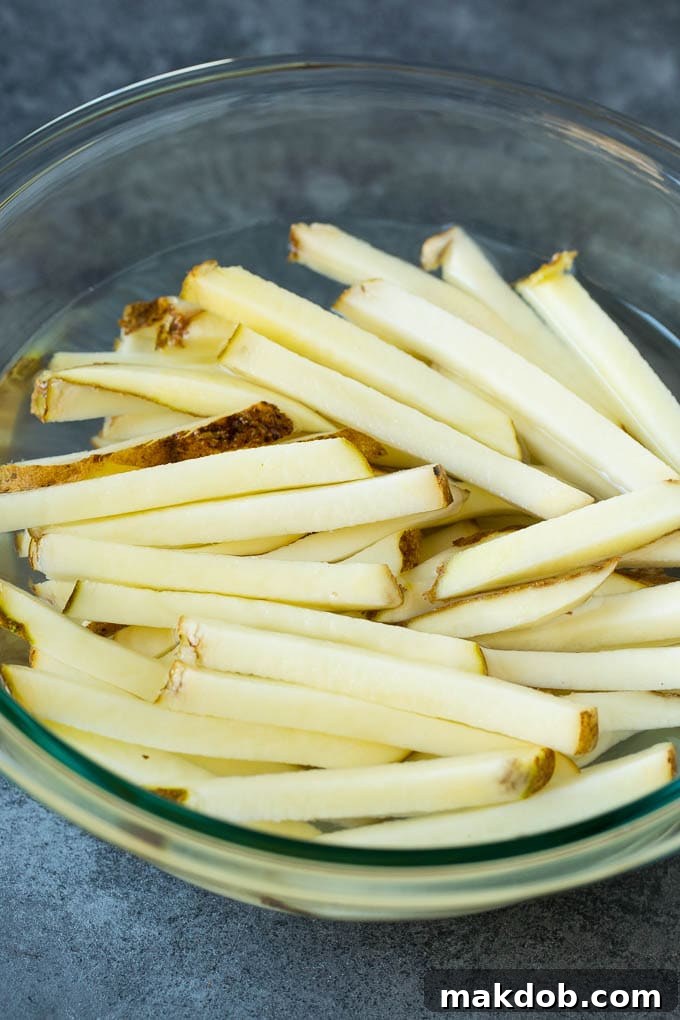 Raw potato matchsticks soaking in a bowl of cold water, a key step for starch removal and achieving crispiness.