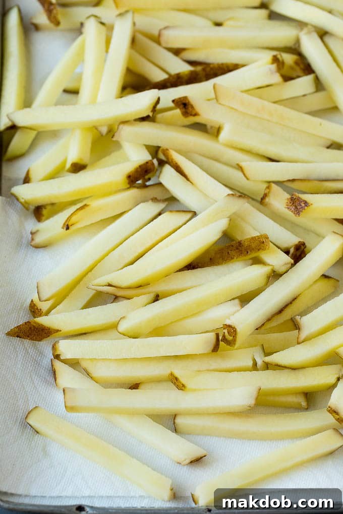 Precisely cut potato sticks drying on a paper towel-lined baking pan, prepared for seasoning and baking.