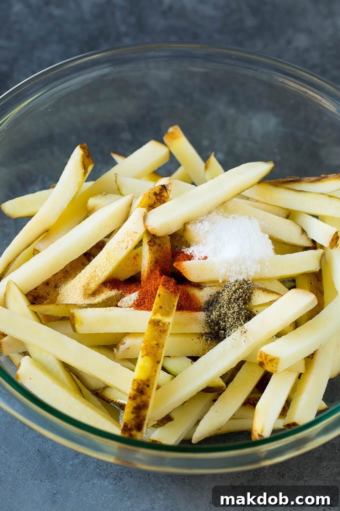 A large mixing bowl filled with raw potato slices thoroughly coated in oil and a vibrant medley of spices.