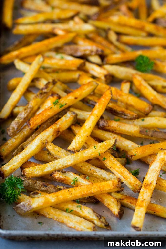 A large sheet pan generously covered with evenly scattered, golden baked french fries, ready for serving.