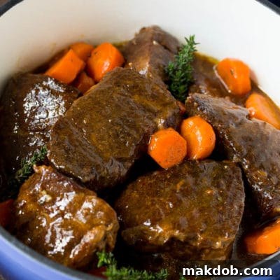 Braised short ribs with carrots in a blue pot, garnished with fresh thyme.