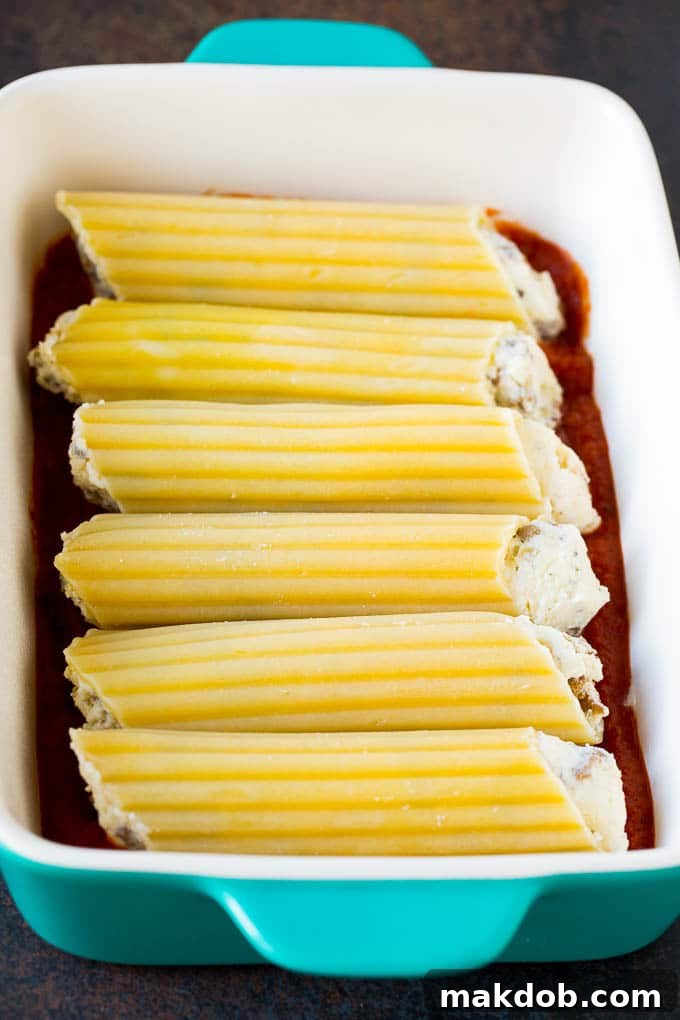 Baked manicotti pasta tubes stuffed with sausage and cheese in a baking dish, covered in marinara sauce.