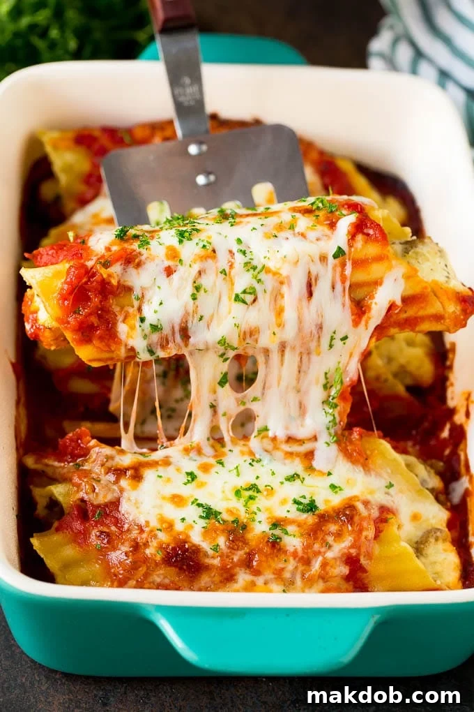 A spatula serving a generous portion of baked manicotti pasta with melted cheese and sauce.
