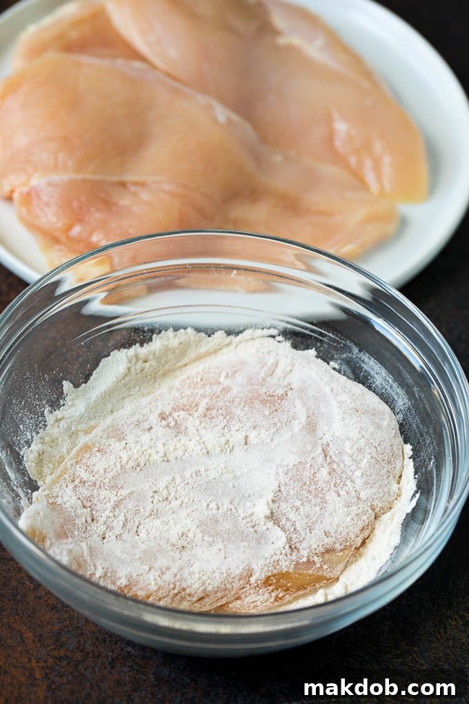 Chicken Scallopini Recipe #chicken #chickenbreast #dinner #dinneratthezoo A chicken breast in a bowl of seasoned flour.