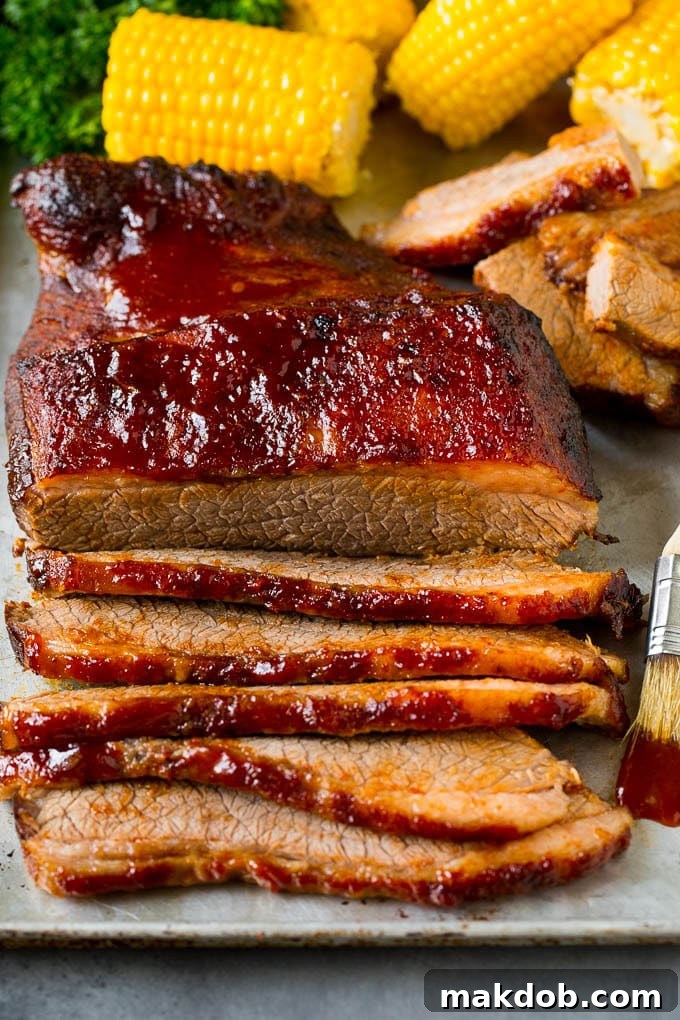 An oven baked beef brisket cut into slices and served alongside corn on the cob, demonstrating perfect tenderness and presentation.