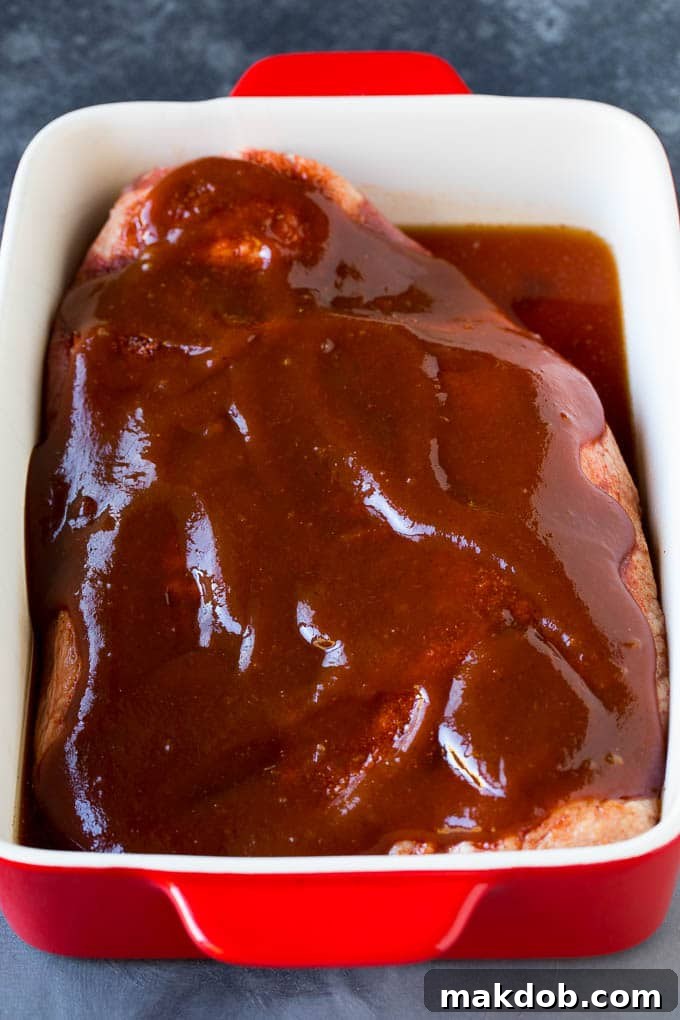 Beef brisket in a baking dish, generously coated with a homemade spice blend and rich barbecue sauce, ready for the oven.