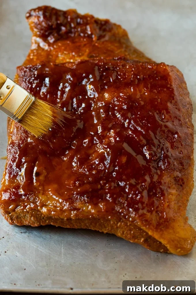 Rich BBQ sauce being meticulously brushed over a perfectly cooked piece of brisket, adding a glossy, flavorful finish.