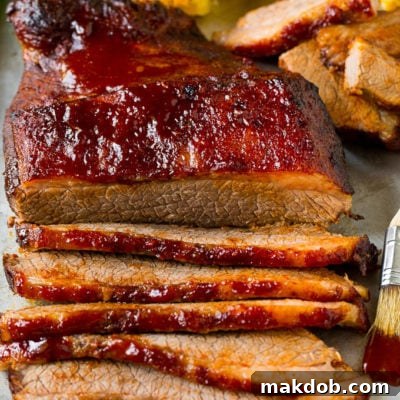 An oven baked beef brisket cut into slices and served alongside corn on the cob.