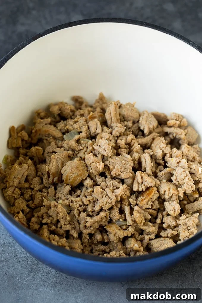 Ground turkey and diced onions being sautéed in a large pot over a stove, preparing the base for turkey chili.