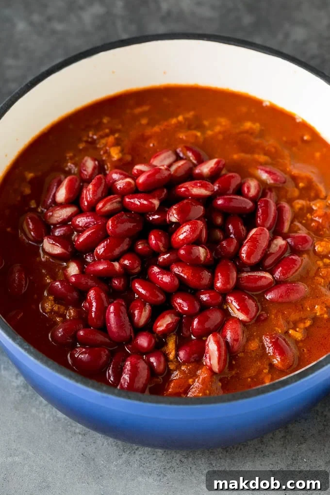 Kidney beans are added to a pot of simmering turkey chili, mixing with the rich tomato sauce and spices.