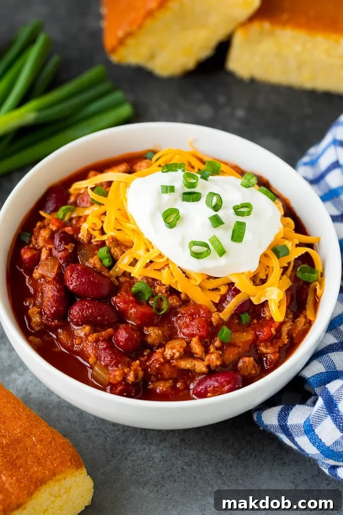 A beautifully presented bowl of turkey chili, generously topped with shredded cheese, a dollop of sour cream, and a sprinkle of vibrant green onions.