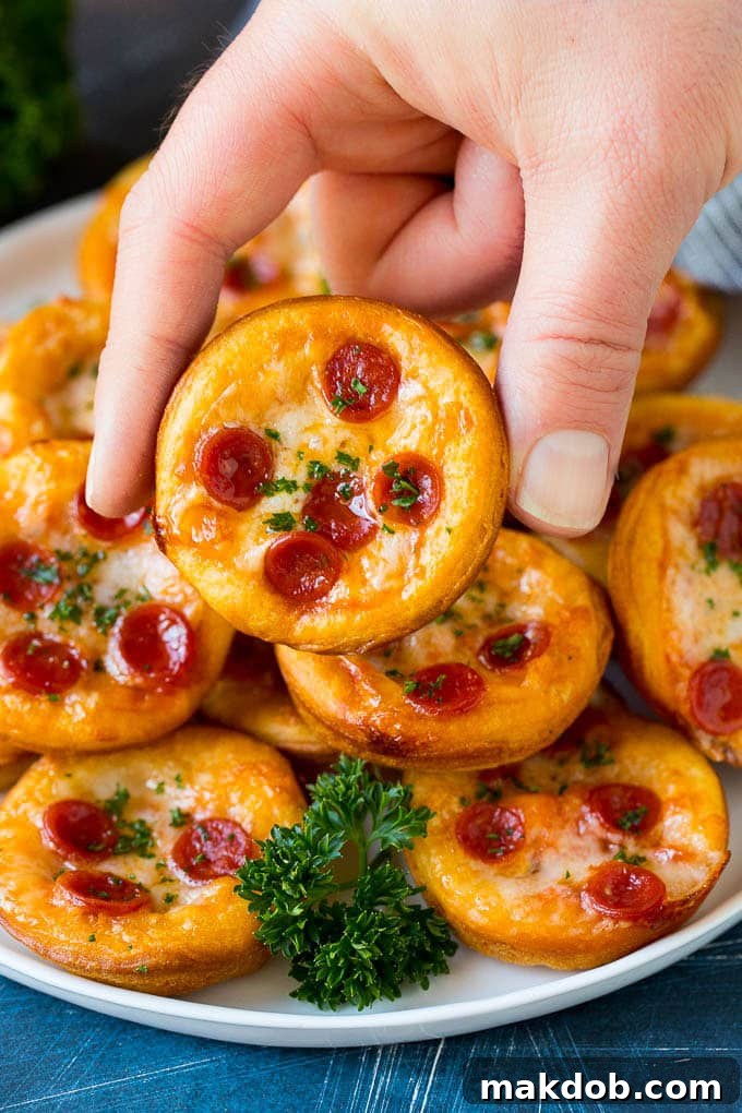 Mini pizzas topped with pepperoni are a fun and easy appetizer option. #pizza #dinneratthezoo #appetizer A platter of mini pizzas with a hand reaching for one.