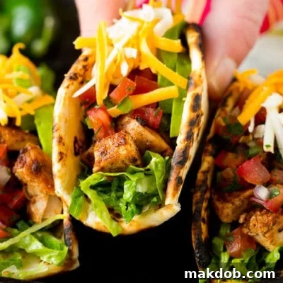 A hand picking up a chicken taco stuffed with meat, cheese and salsa.
