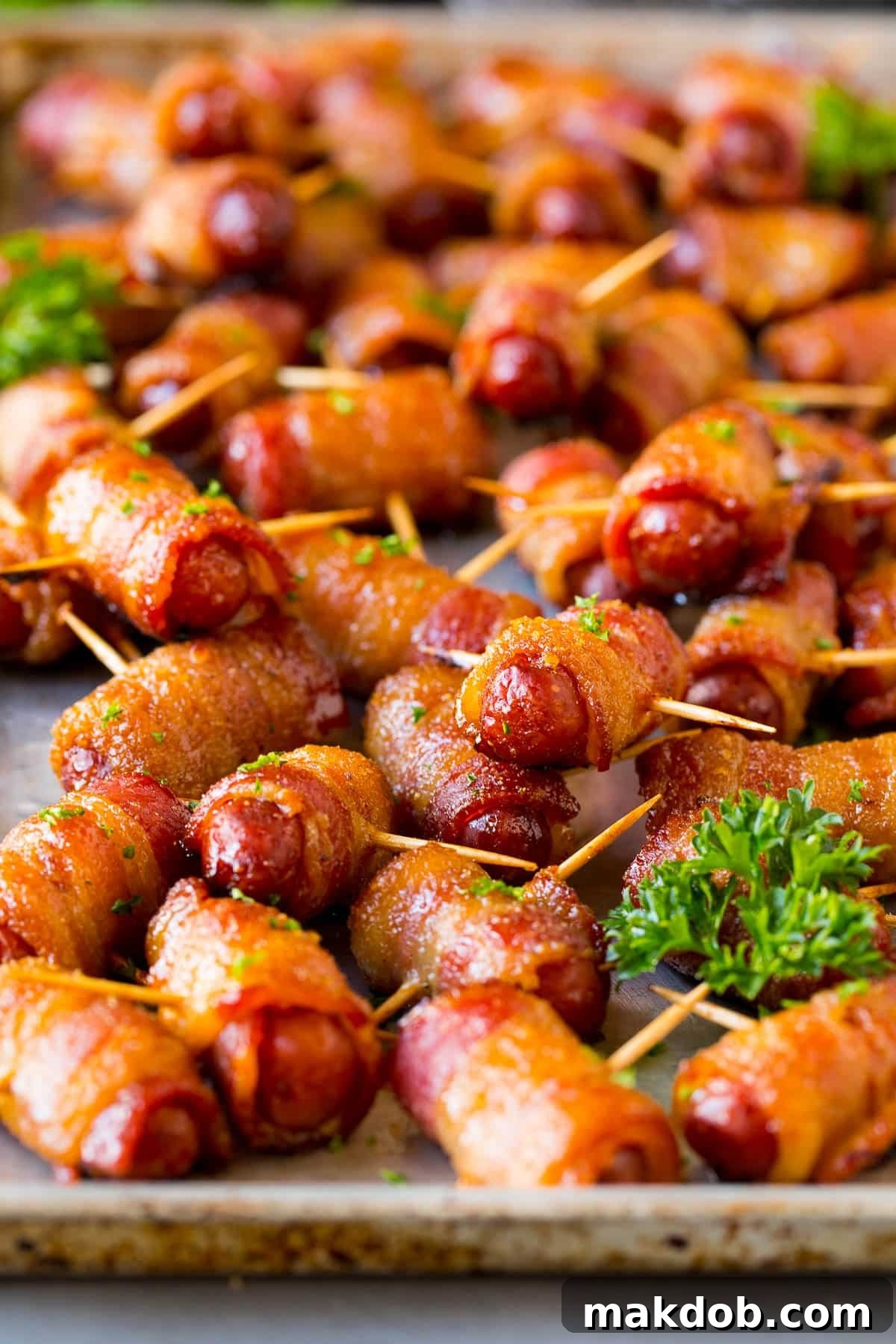A sheet pan generously filled with perfectly cooked bacon wrapped smokies, beautifully caramelized and garnished with fresh parsley.