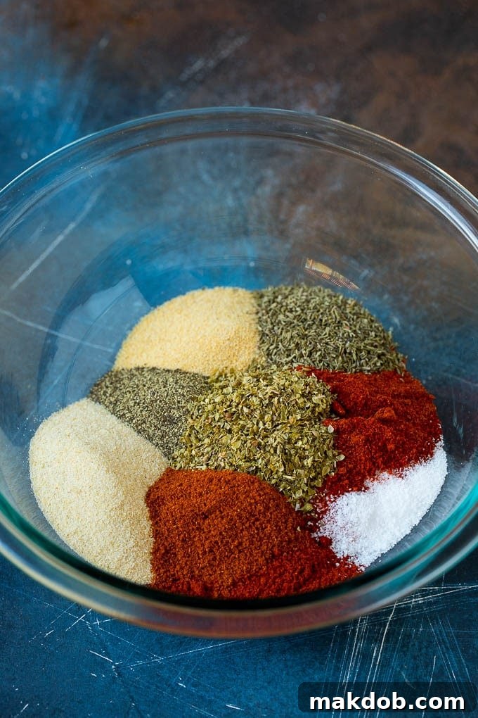 Homemade Cajun seasoning made with a unique blend of herbs and spices. #cajun #dinneratthezoo A mixing bowl containing various powdered spices like paprika, garlic powder, onion powder, and dried herbs, partially combined.
