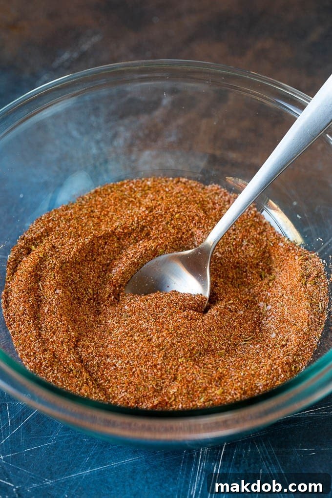Homemade Cajun seasoning made with a unique blend of herbs and spices. #cajun #dinneratthezoo A close-up shot of various mixed spices, including red paprika, black pepper, and green herbs, forming a rich seasoning blend in a bowl.