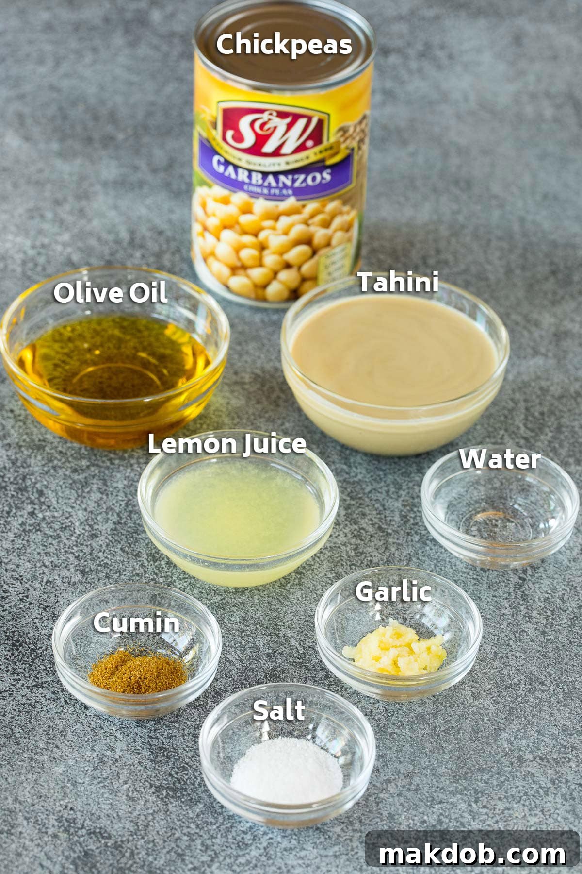 Ingredients for creamy hummus: a can of chickpeas, lemon juice, tahini, olive oil, and spices laid out on a table.