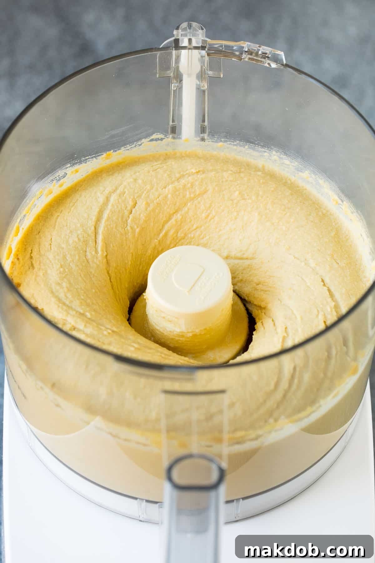 Close-up of chickpeas and tahini being blended together in a food processor, highlighting the start of creamy hummus.