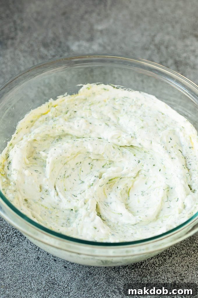 A close-up shot of creamy tzatziki sauce presented in a clear glass bowl, showcasing its smooth texture and fresh herbs.
