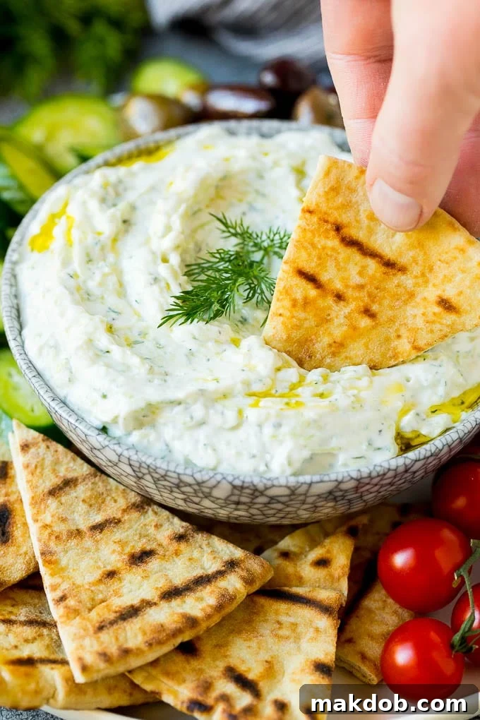 A hand dipping a piece of pita bread into a bowl of creamy, homemade tzatziki sauce, highlighting its perfect dipping consistency.