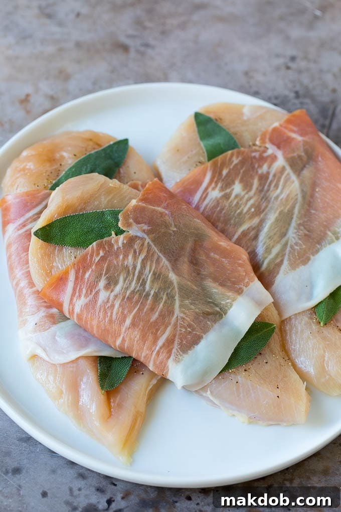 Raw chicken cutlets topped with fresh sage leaves and wrapped in prosciutto slices.