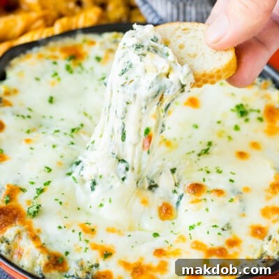 A slice of bread scooping up a serving of spinach artichoke dip.