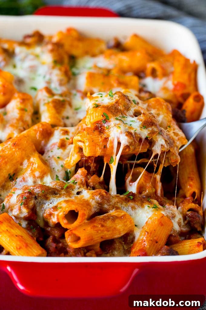 Hearty Pasta al Forno with Rigatoni and Sausage A spoon serving up a portion of Pasta al Forno with rigatoni and sausage, showcasing melted cheese and rich sauce.