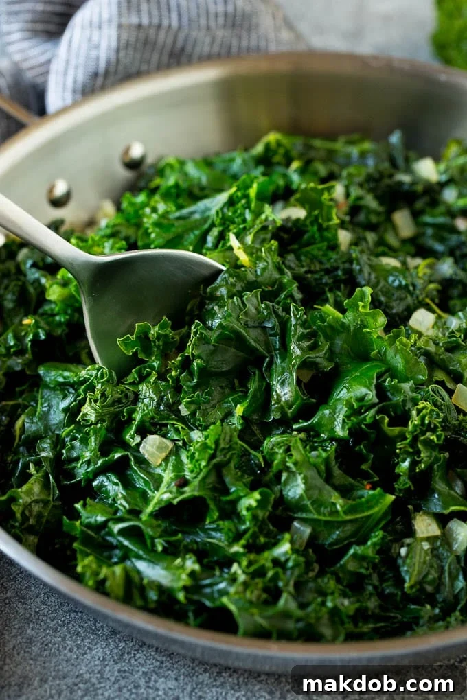 A pan of tender sauteed kale with a serving spoon, garnished with fresh herbs.