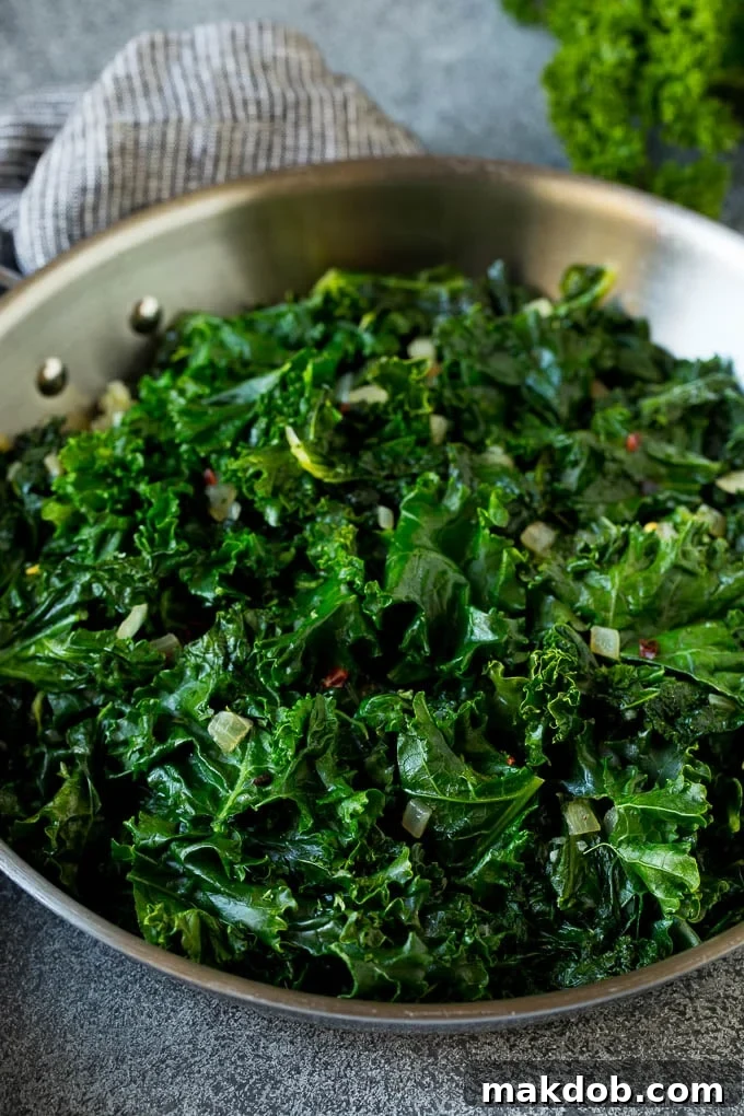Close-up shot of cooked kale glistening with olive oil, mixed with tender onions and fragrant garlic, showcasing its tender texture.