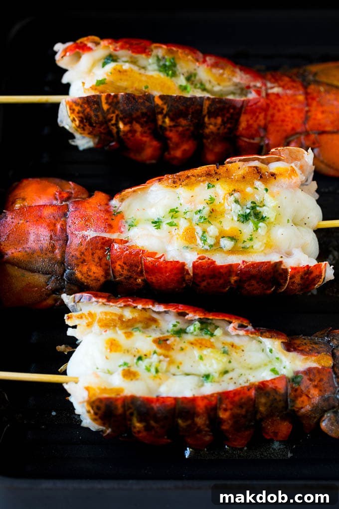 Cooked lobster tails resting on a grill pan, beautifully brushed with rich butter and ready to serve.