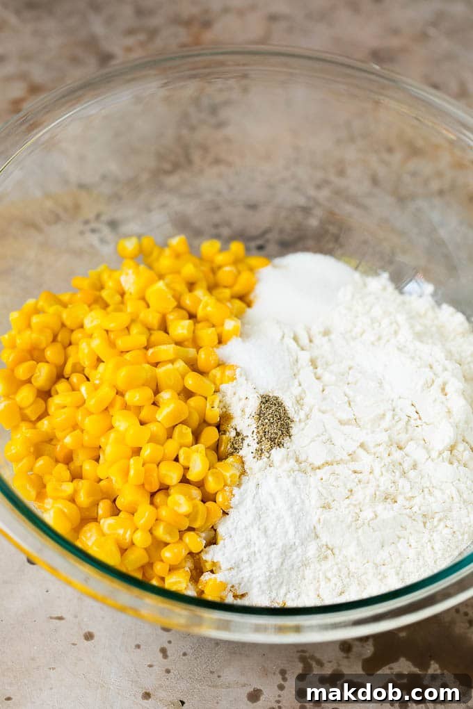 Flour, corn, and seasonings are carefully mixed in a bowl, showing the initial stages of preparing the corn fritter batter.