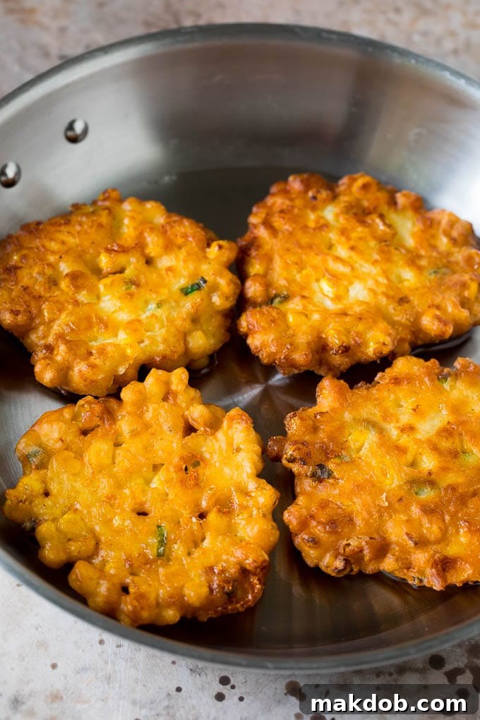 Golden-brown corn cakes sizzling in a hot pan of oil, cooking to perfection.